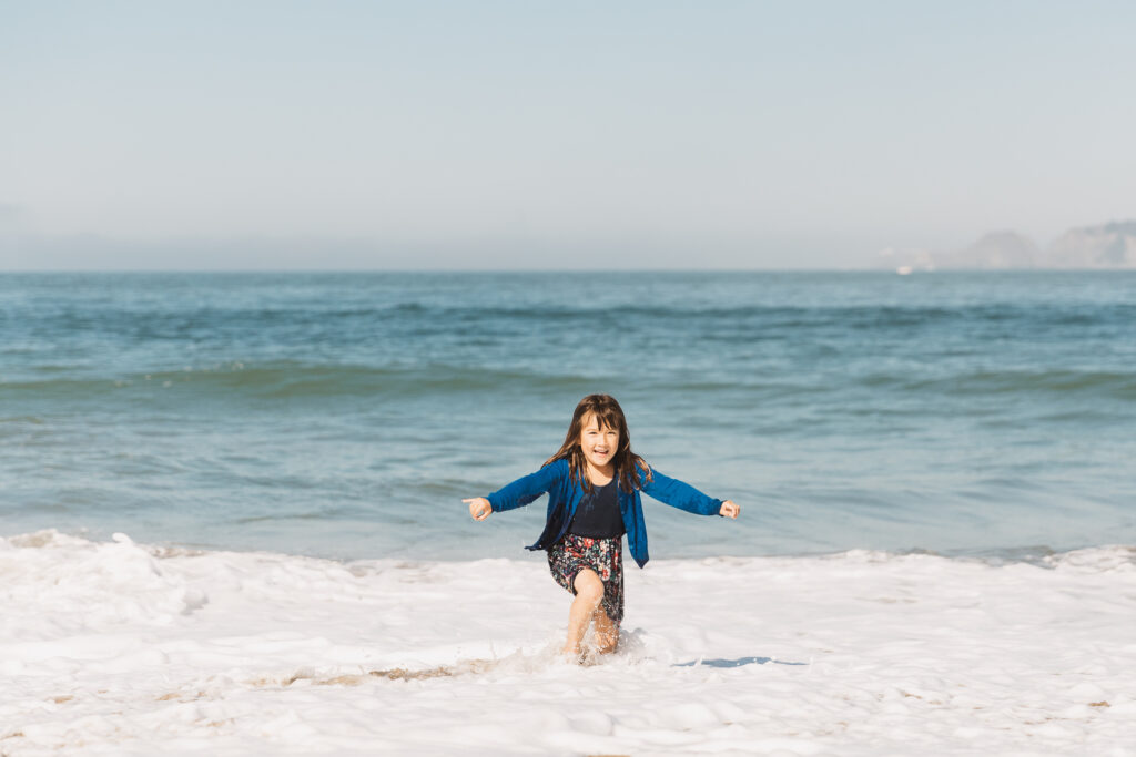 Girl jumping the waves at Baker Beach during a family photo session.
