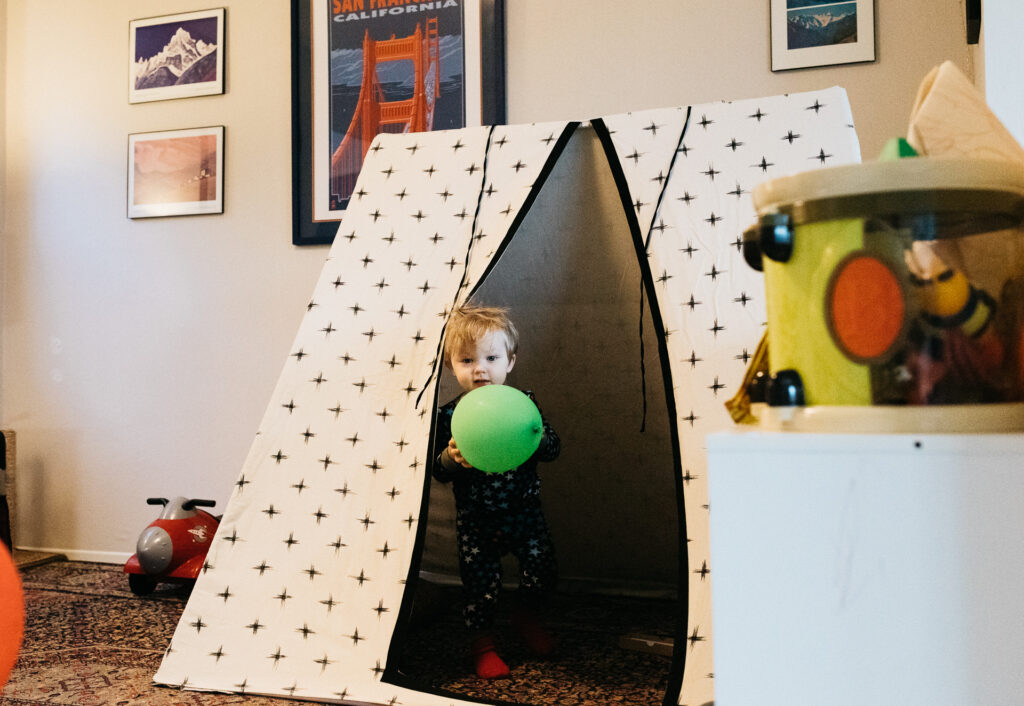 toddler boy holding a balloon inside a play tent during a family photo session in oakland.