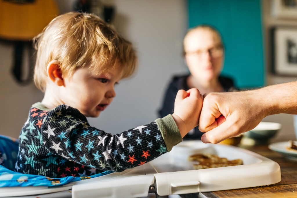 toddler boy fist bumping at the breakfast table during an in-home photo session in oakland.