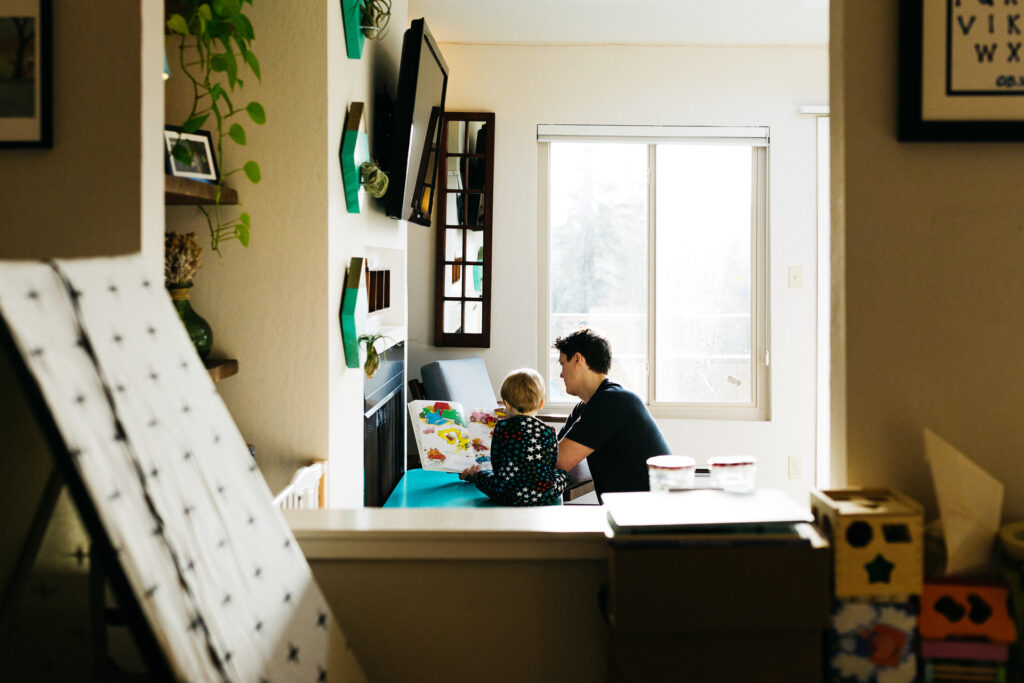 dad reading a book to his toddler son during a family photo session at home in oakland.