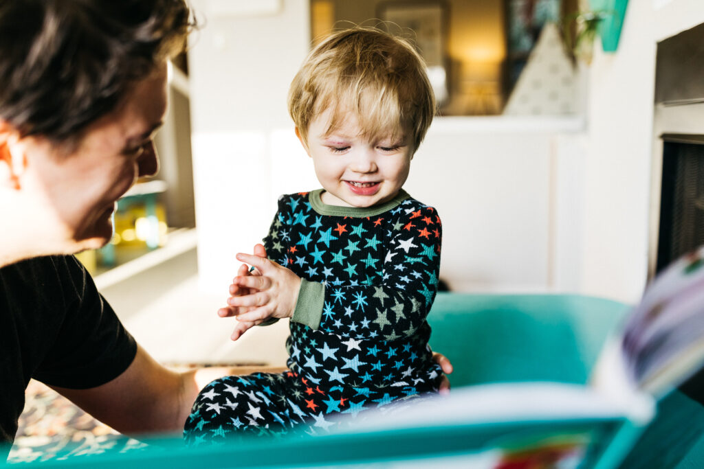 boy smiling while his dad reads to him at home.