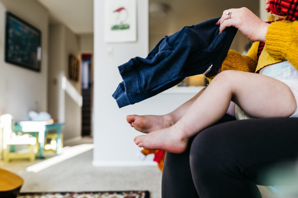 dad putting clothes on his son during an in-home photo session in oakland.