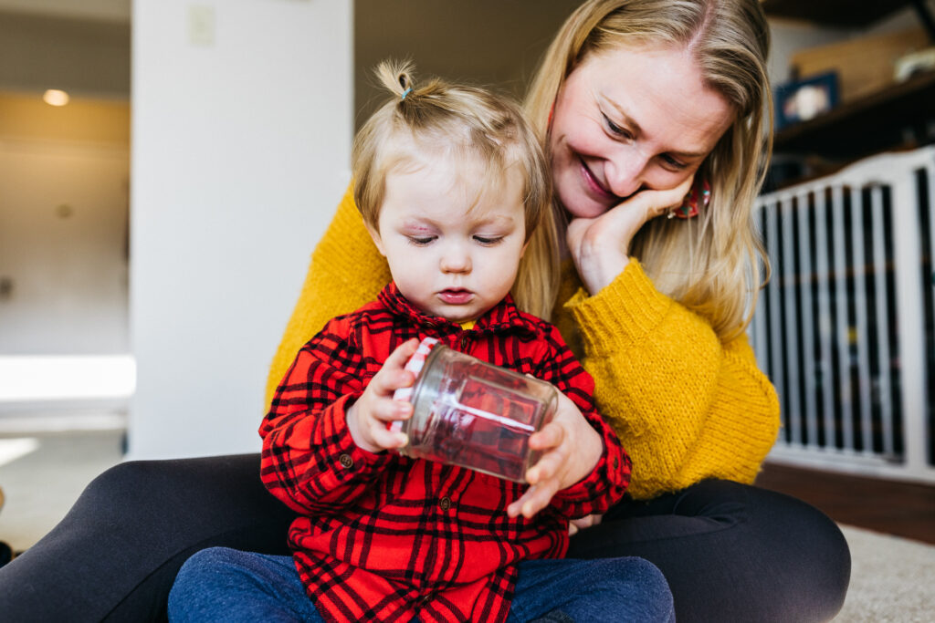 mom smiling and basking in joy while watching her son play with a glass jar.