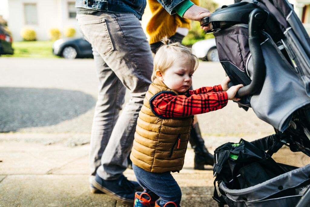 toddler boy pushing his stroller during a family walk in oakland.