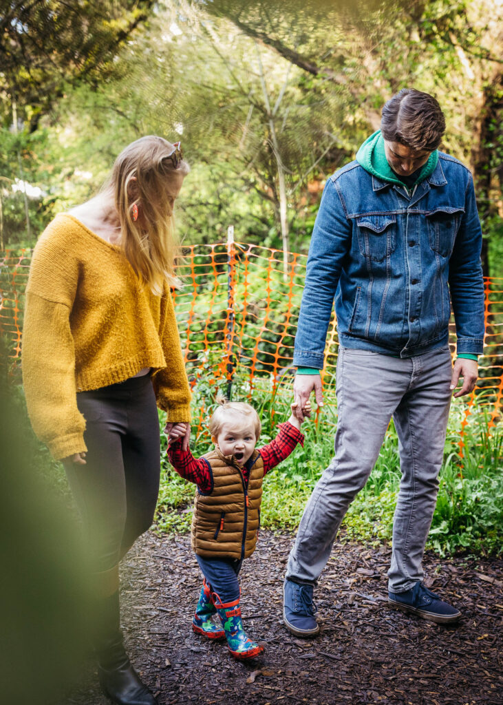 mom and dad with their young son on a walk in an oakland park.
