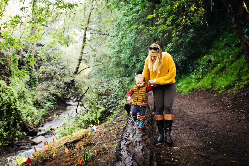 mom holding young son while he balances on a fallen log.