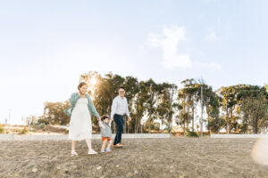 pregnant mom is walking with toddler daughter and husband on the beach.