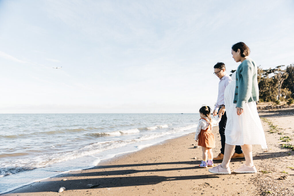 Family of three holding hands and watching the waves and plane on the beach.