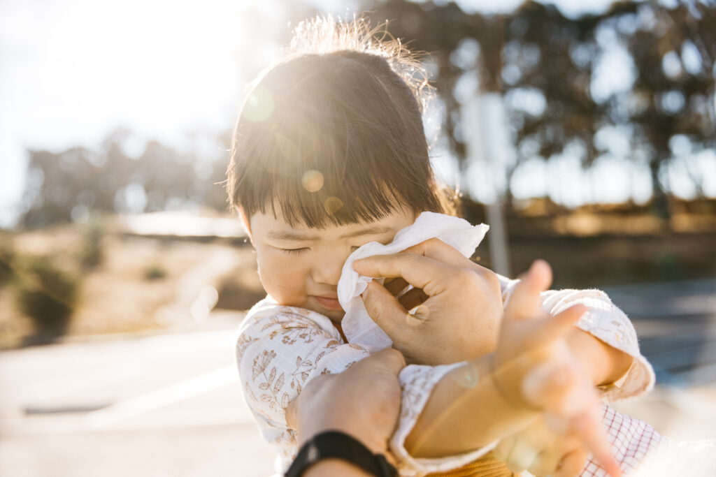 Toddler girl is resisting the kleenex as her dad wipes her face.