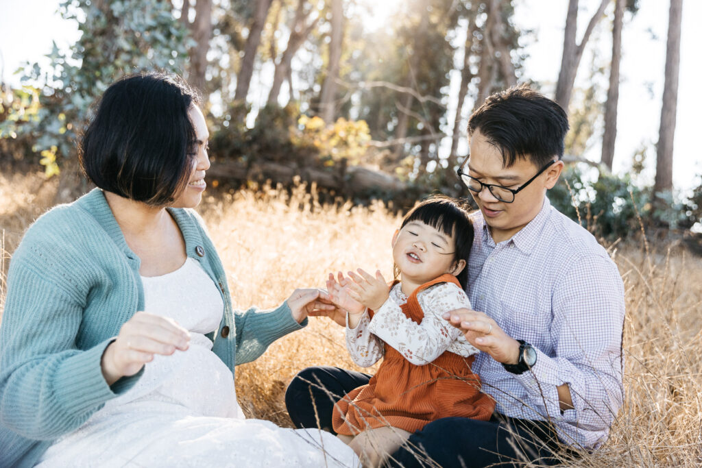 Family of three are singing while sitting in the grass.