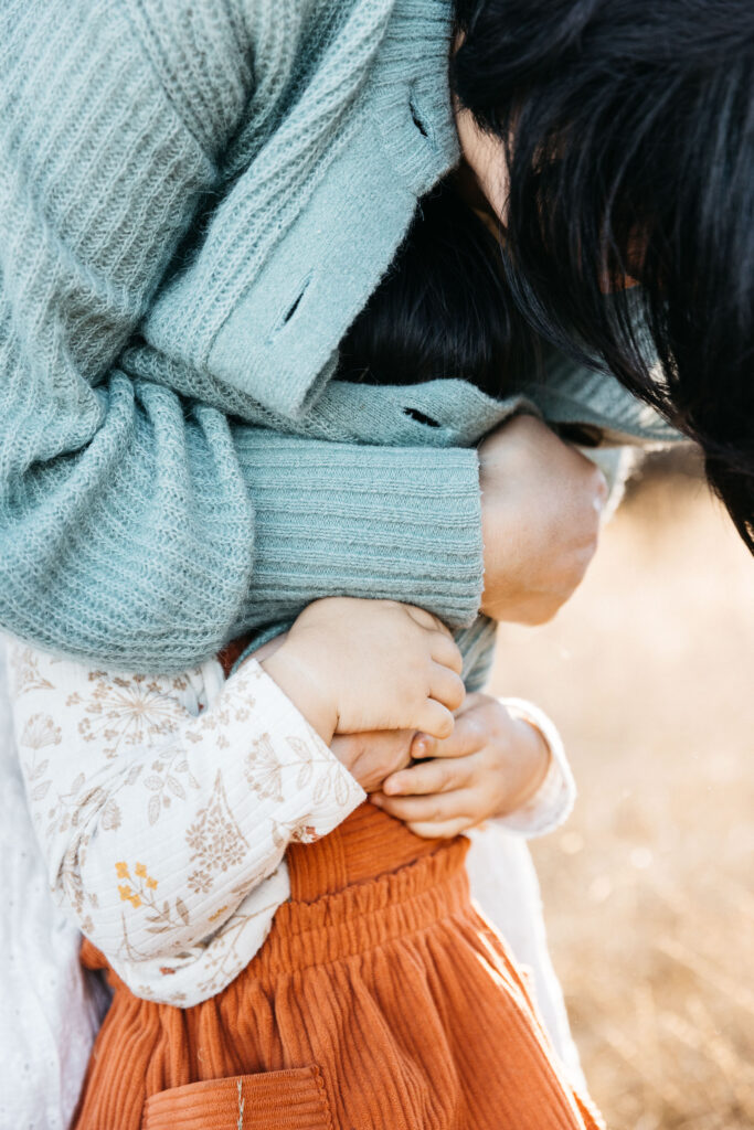 Mother is using her cardigan to play peek-a-boo with her toddler daughter.