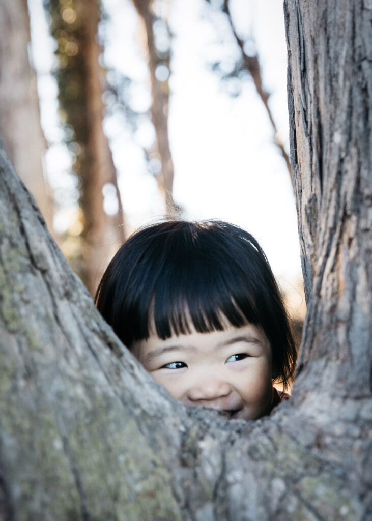 Toddler girl is playing hide and go seek with a tree at coyoto point. park.