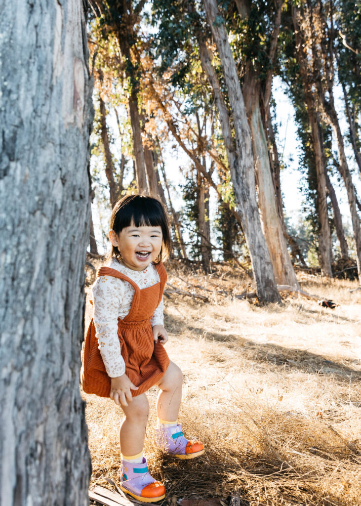 Toddler girl is laughing while playing peek a boo at Coyote Point.