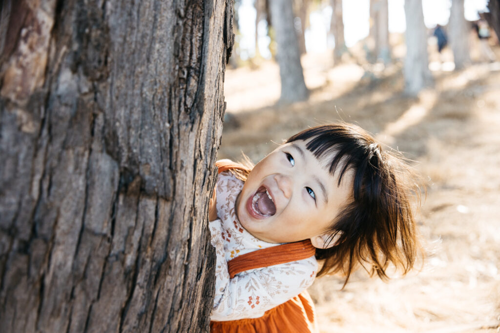 Toddler girl is laughing and having fun while playing peek a boo at Coyote Point.