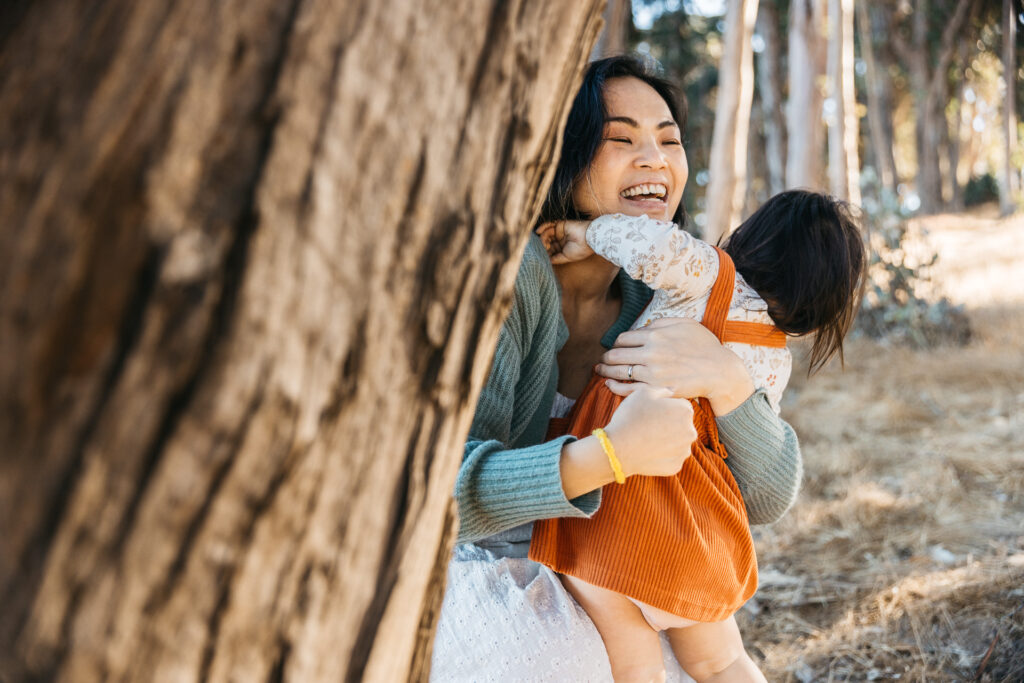 Mother smiles as her toddler daughter runs and hugs her.