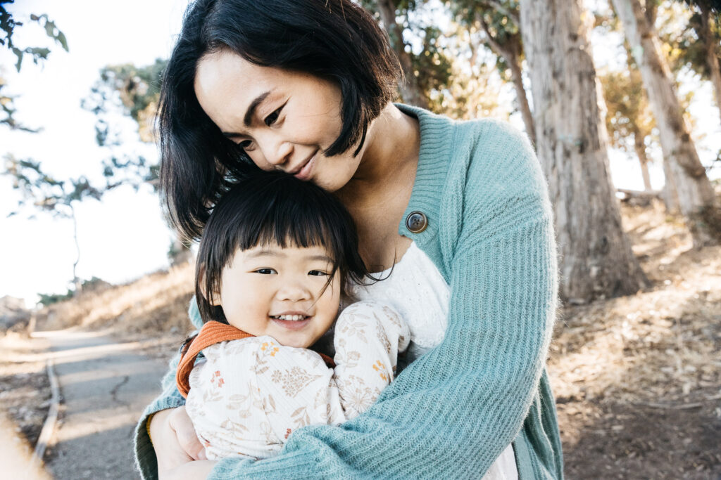 Pregnant woman smiles as she hugs toddler daughter.