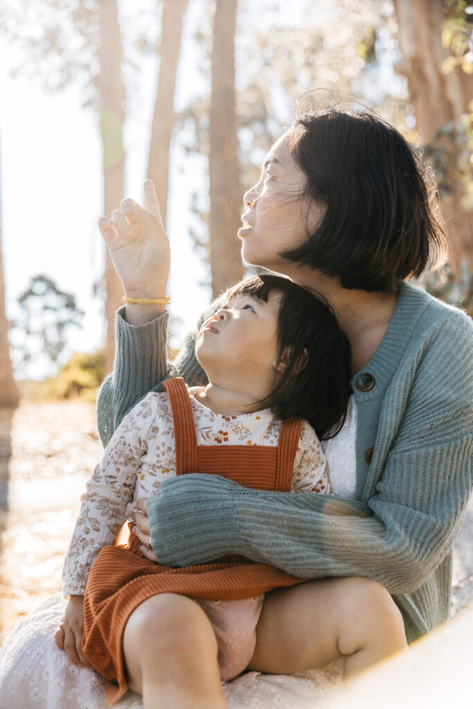 Pregnant woman points to a plane in the sky to her toddler daughter.