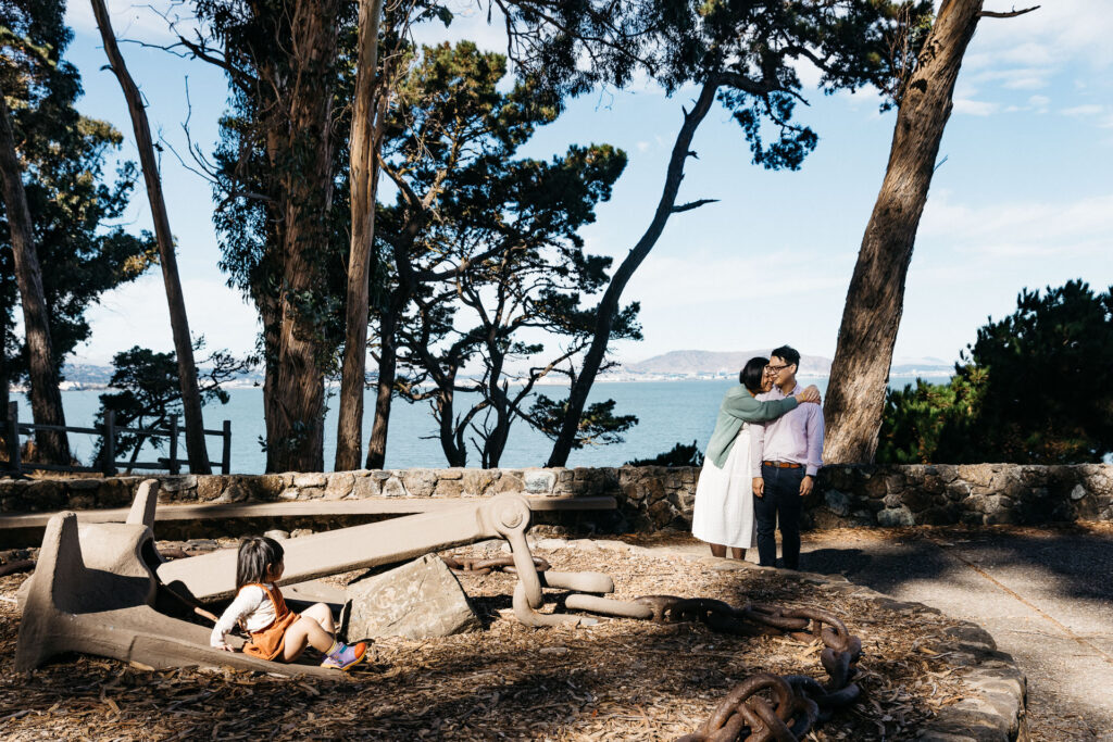 Mother and father sharing a tender moment hugging as their toddler daughter watches them.