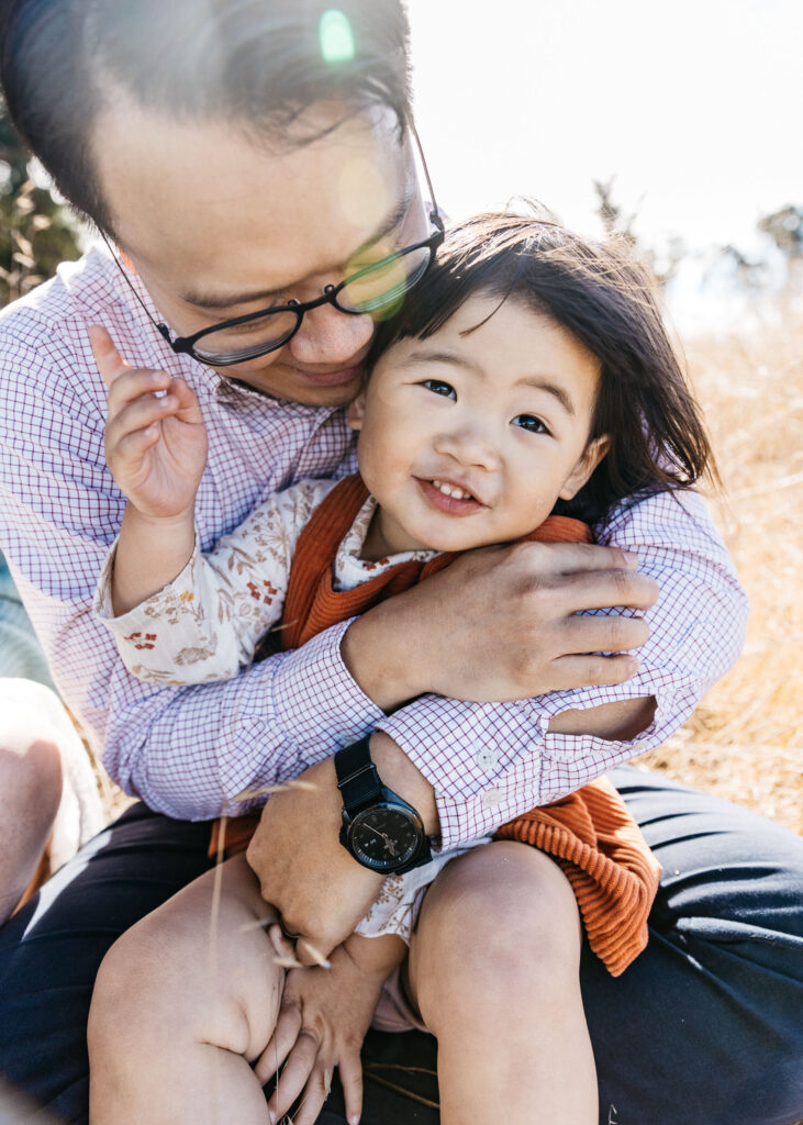 Dad tenderly holding his toddler daughter in the grass.