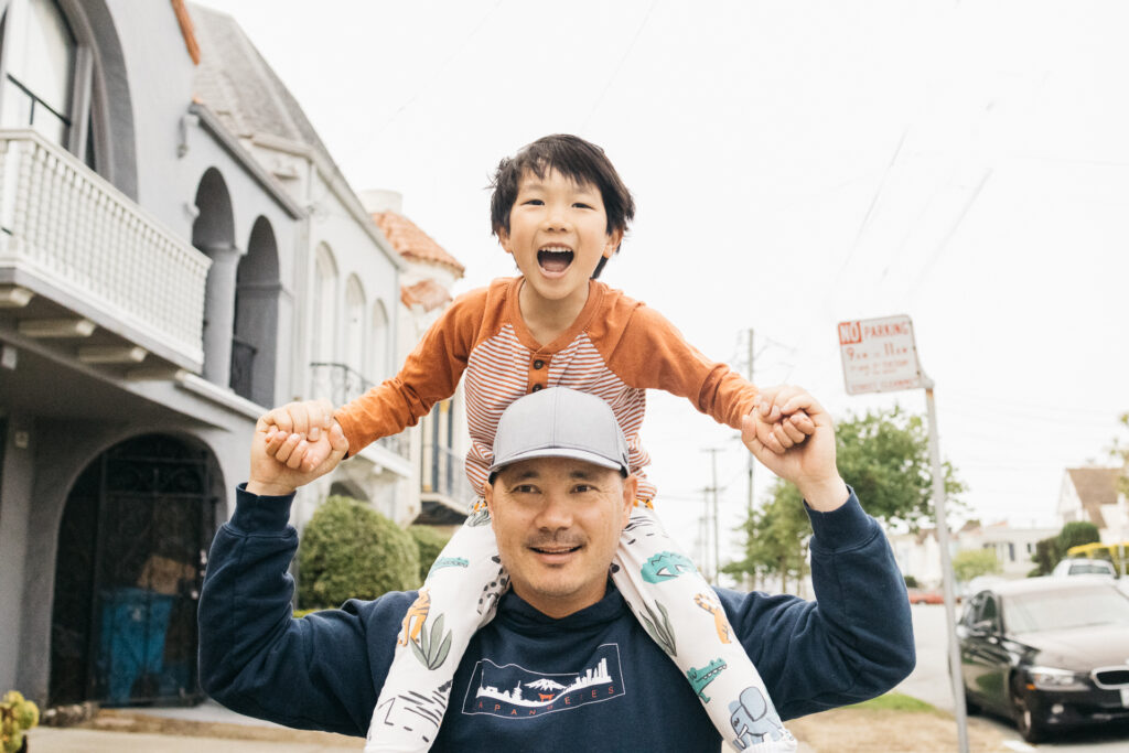 dad carrying toddler son on his shoulders in the sunset neighborhood of san francisco.