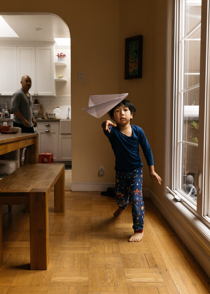 toddler boy throwing a paper airplane at home.
