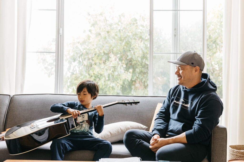 Toddler boy learning to play dad's acoustic guitar.