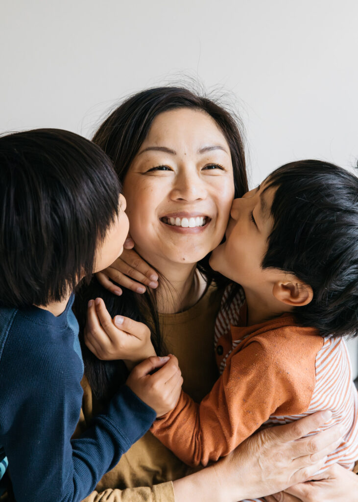 toddler brothers kissing mom on the cheek.