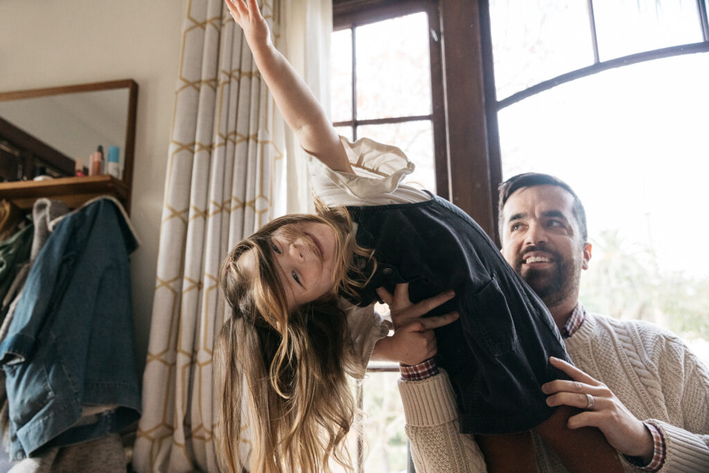 toddler girl balancing on her dad's hand in the living room during a family photo session in oakland.