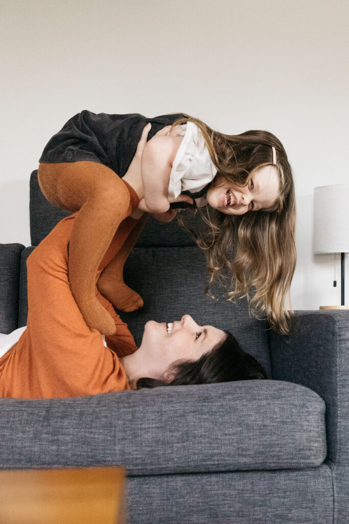 mom carrying young daughter on the sofa during a family photo session in oakland.
