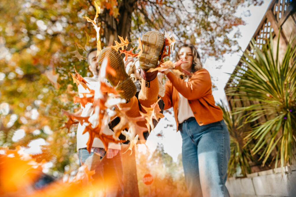 mom and dad swinging young daughter in a pile of fall leaves.