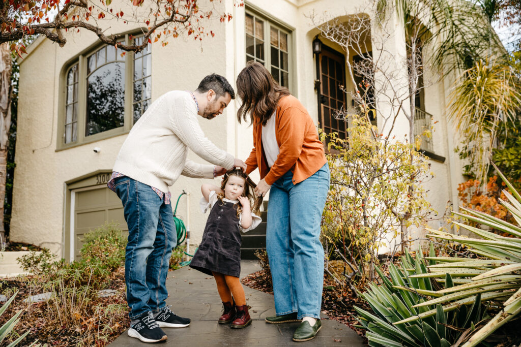 mom and dad fixing young daughter's hair in front of their home.