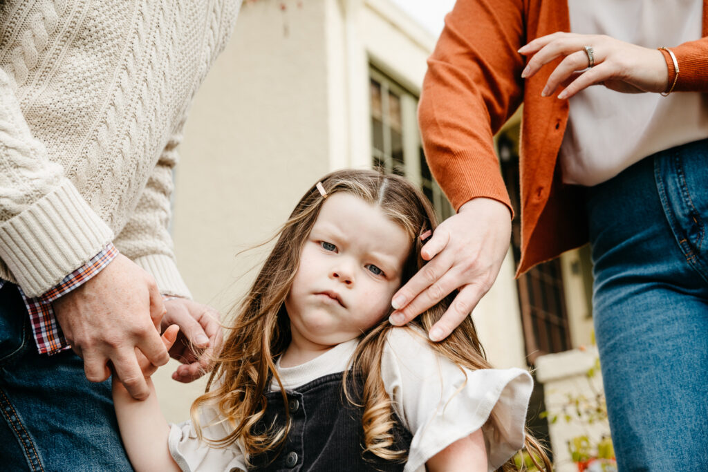 young girl pouting while mom and dad adjust her hair.