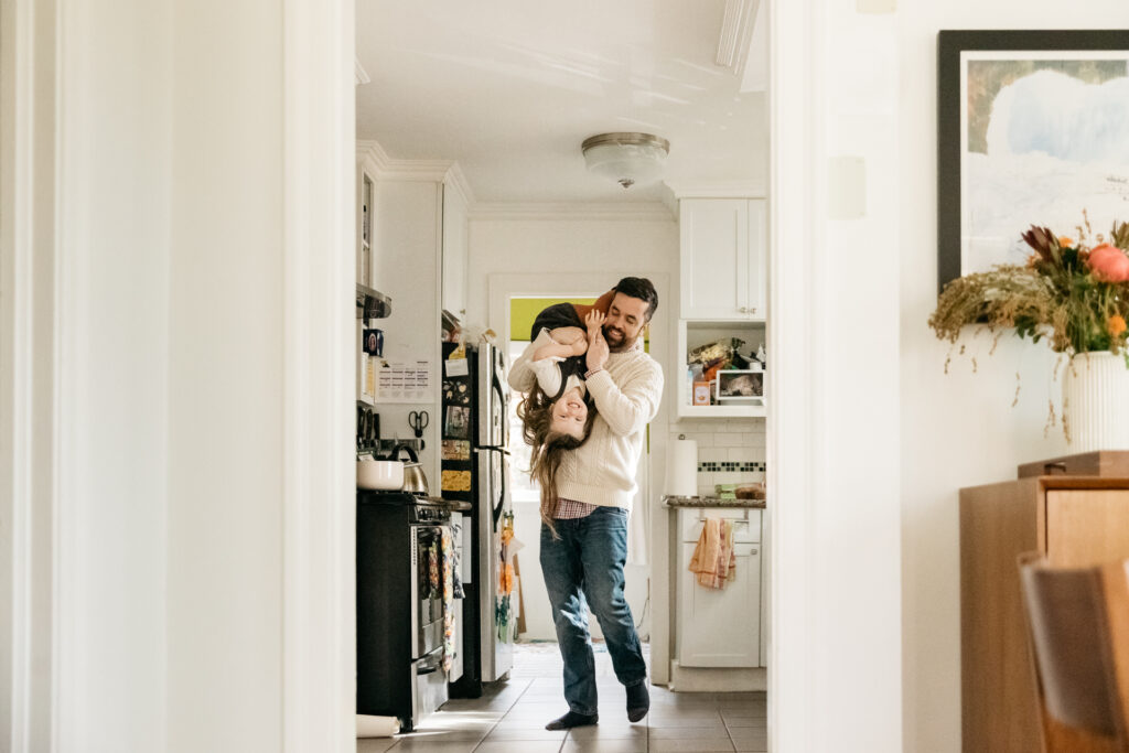 dad carrying daughter upside down on his shoulders in the kitchen.