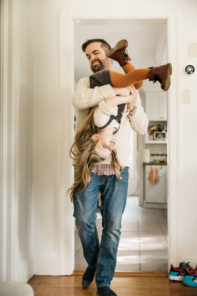 dad carrying daughter upside down on his shoulders in the kitchen.