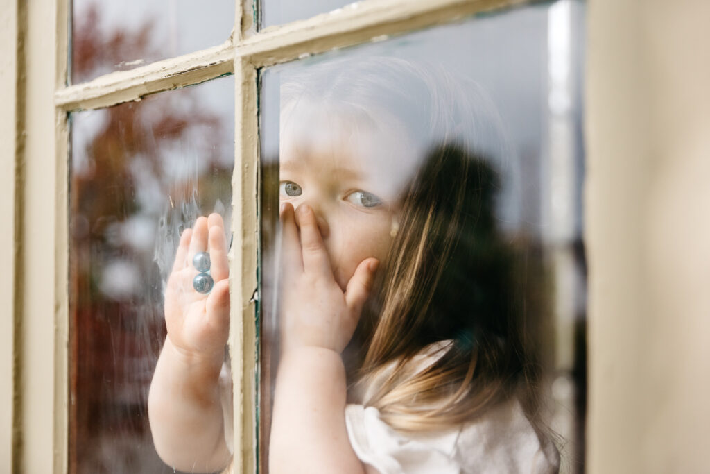 young girl looks out the window while blowing kisses.