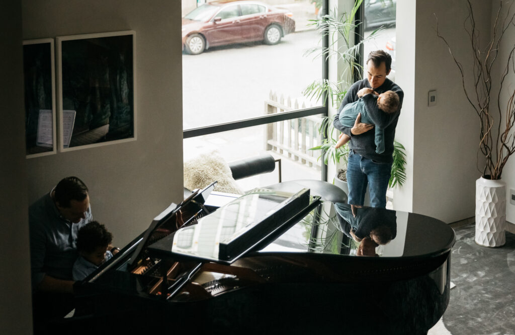 dads hanging out in the living room playing the piano with kids.