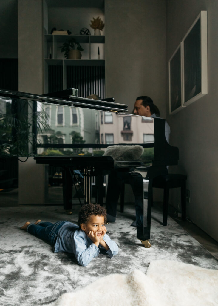young toddler boy laying under the piano while his dad plays.