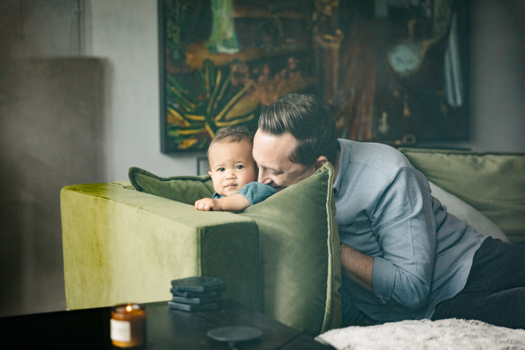 dad cuddling with young toddler daughter on the sofa during an in-home family photo session in san francisco.