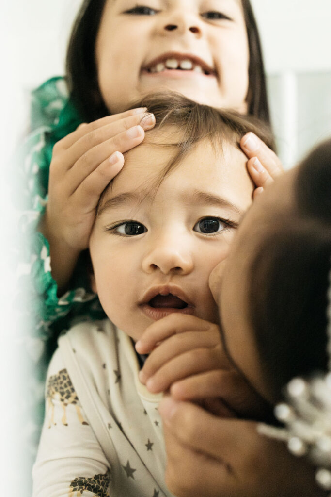 Sisters are attacking baby brother with hugs and kisses.