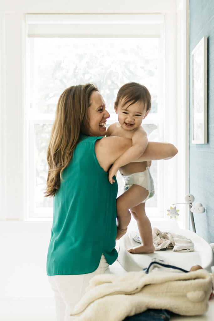 Mom is cuddling with her young son as he stands on the changing table in his nursery.