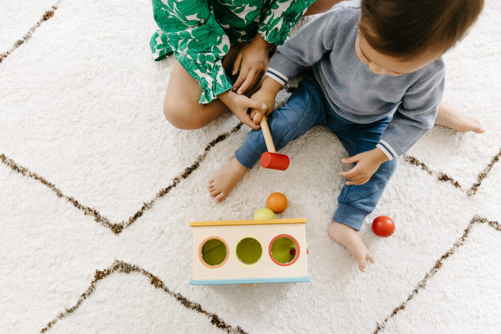 Older sister is teaching her toddler brother how to play with a toy hammer and balls.