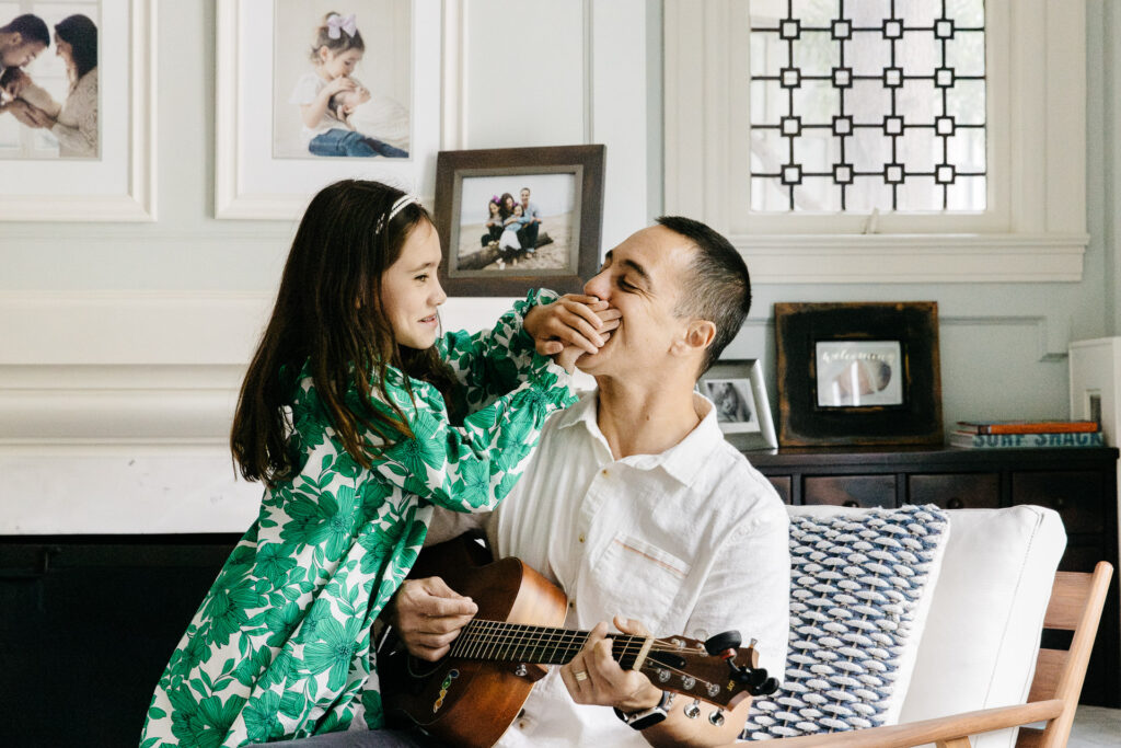 Nine year old is putting her hand over her dad's mouth to stop him from singing.
