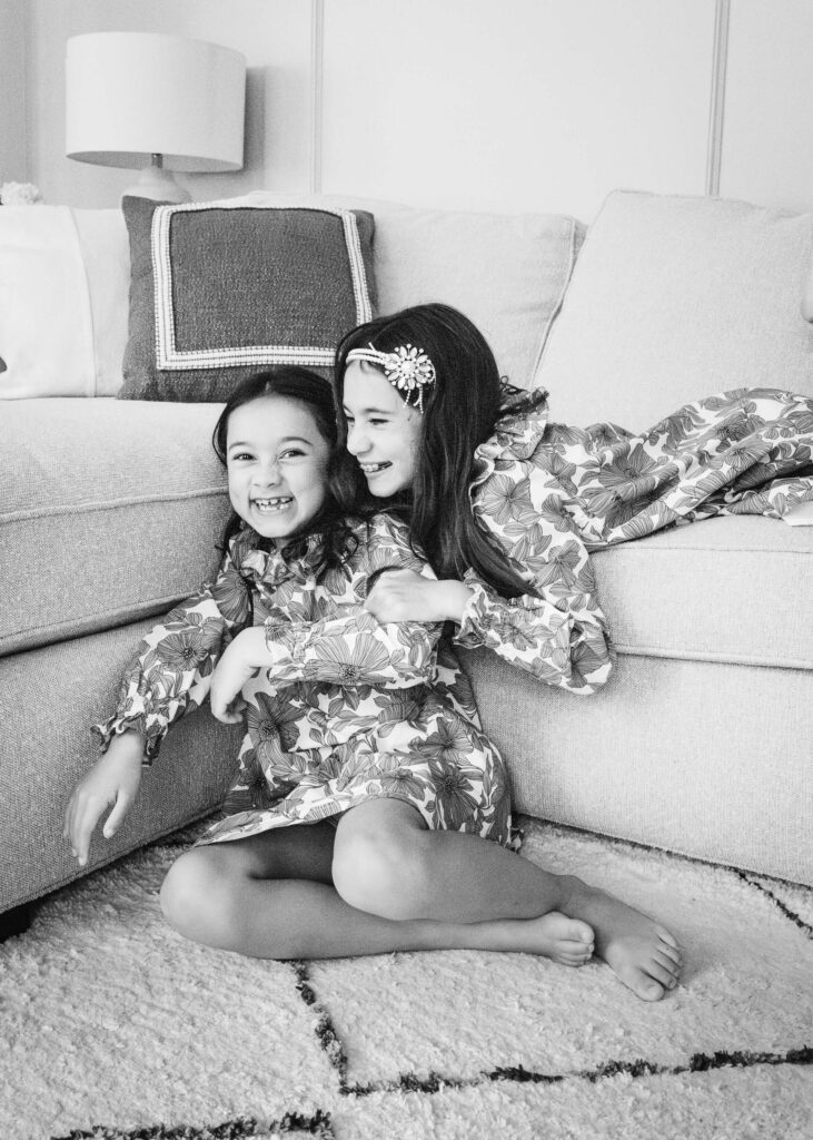 Sisters are hugging and laughing on the sofa.