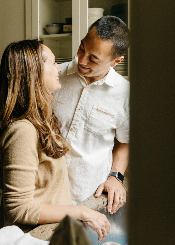 A couple is sneaking glances at each other sweetly in the kitchen.