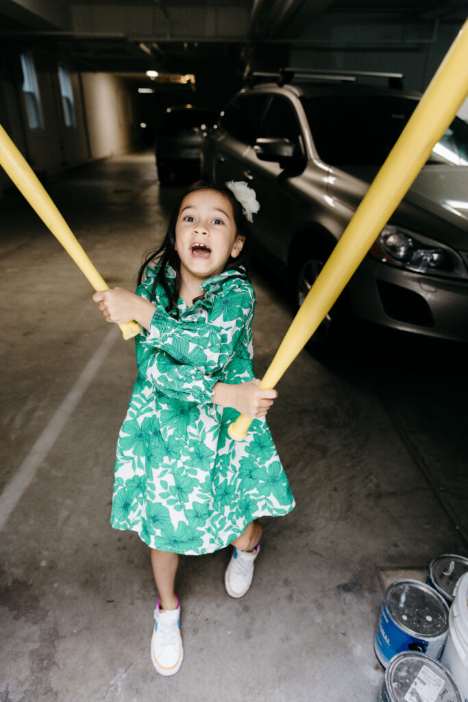 Eight year old girl is swinging plastic baseball bats like nunchakus.