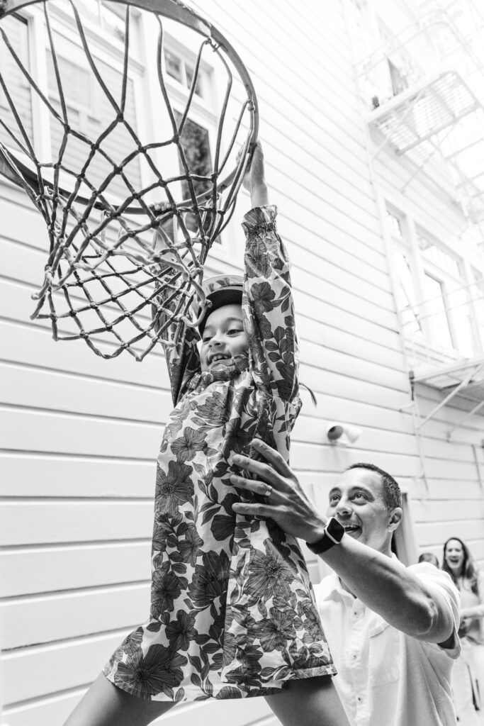 Dad helps his daughter with a slam dunk by carrying her to the net.