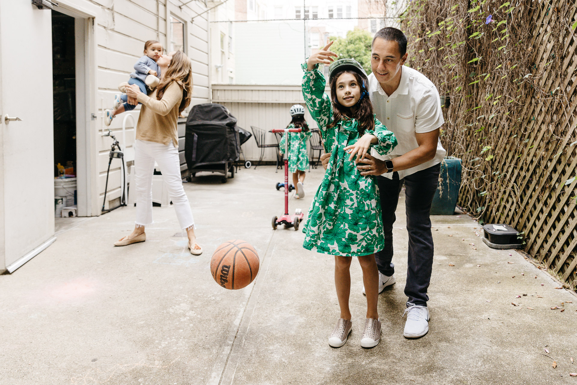 Dad guides his daughter to shoot a basket in the backyard.