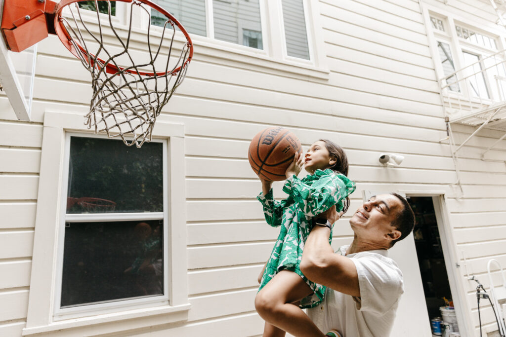 Dad helps daughter shoot a basket by carrying her close to the net.