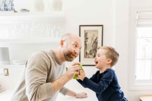 Dad is laughing with his toddler son in the kitchen during a family photo session at home in Piedmont.