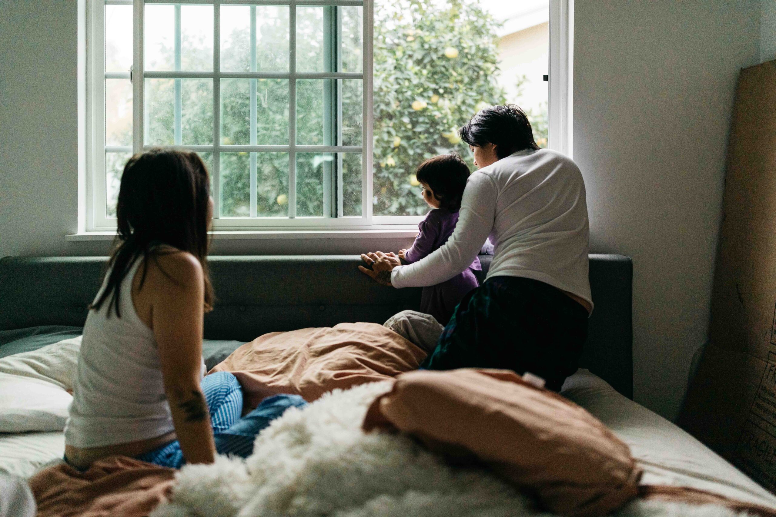 Mom is quietly watching her husband play with their child at the bedroom window.